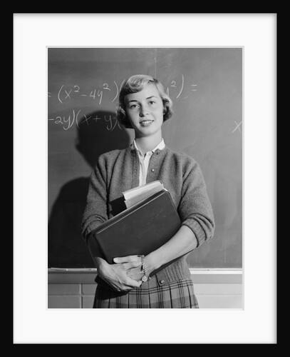Teenage girl holding school books standing in front of blackboard by Anonymous