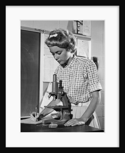 Teen girl writing notes working with microscope in science classroom by Anonymous