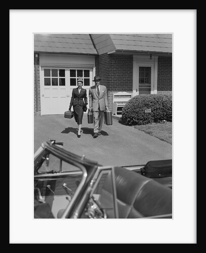 Couple carrying luggage walking towards convertible car in driveway by Anonymous