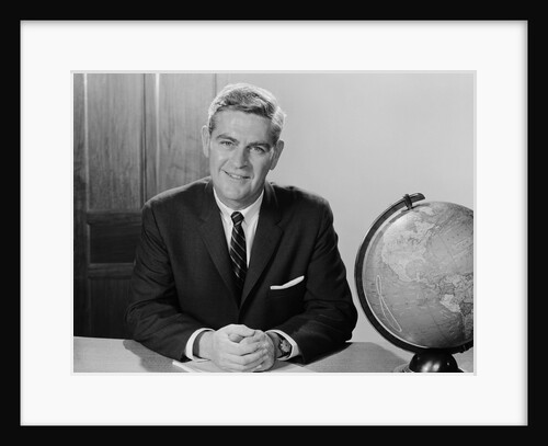 Smiling man sitting at desk with earth globe by Anonymous