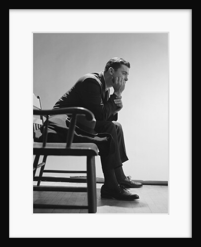 Sad man resting hand on chin sitting on bench by Anonymous