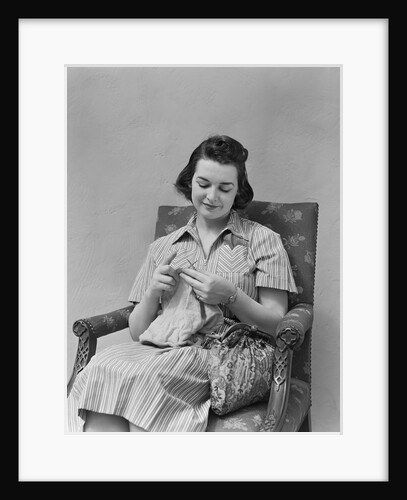 Brunette woman knitting sitting in armchair by Anonymous