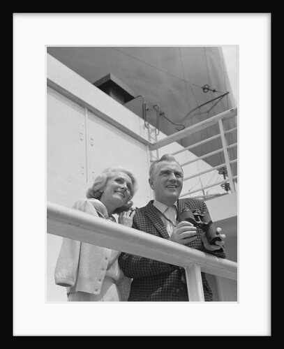 Smiling mature couple at shipboard rail with binoculars by Anonymous