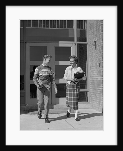 Two teenage students boy and girl walking away from school doors carrying books by Anonymous