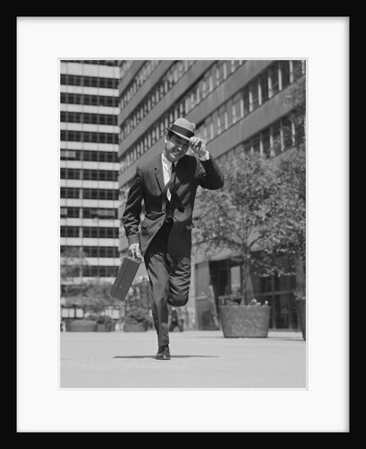 Businessman carrying briefcase holding his hat on running down urban sidewalk by Anonymous