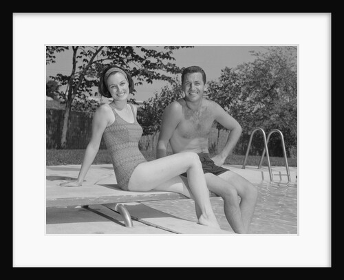 Man woman couple sitting on diving board on side of swimming pool by Anonymous
