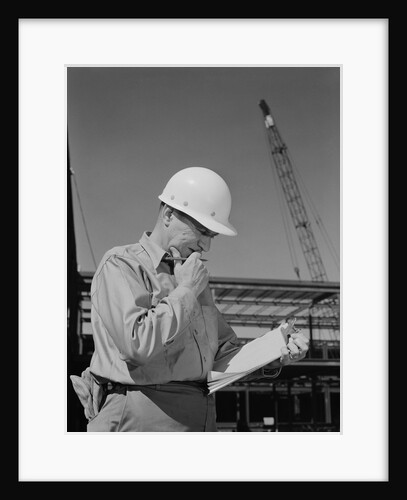 Male construction site supervisor wearing hard hat reading papers by Anonymous