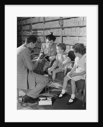 Family mother two children in shoe store trying new shoes helped by salesman by Anonymous