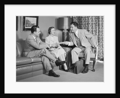 Couple sitting on couch talking to smiling insurance salesman handing them a policy by Anonymous