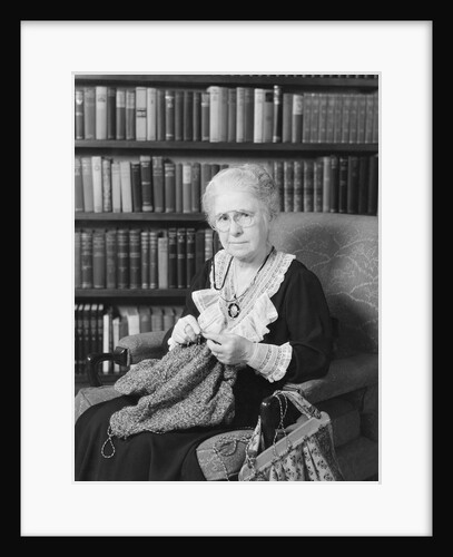 Elderly woman sitting before bookcase serious expression knitting by Anonymous