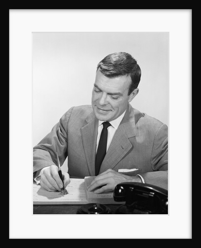 Smiling businessman at desk writing checks by Anonymous