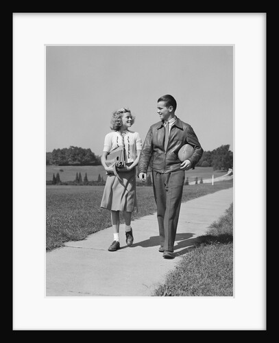 Teen couple walking down sidewalk girl with school books boy holding football by Anonymous