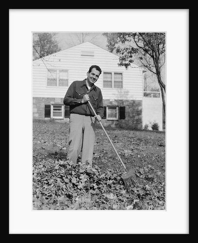 Smiling man raking autumn leaves in front yard of house by Anonymous