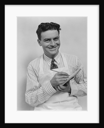 Smiling curly hair man wearing apron taking order with pencil and note pad by Anonymous