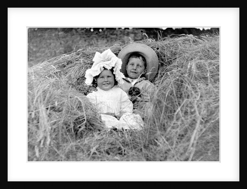 A young brother and sister nestled in the hay, ca. 1900. by Anonymous