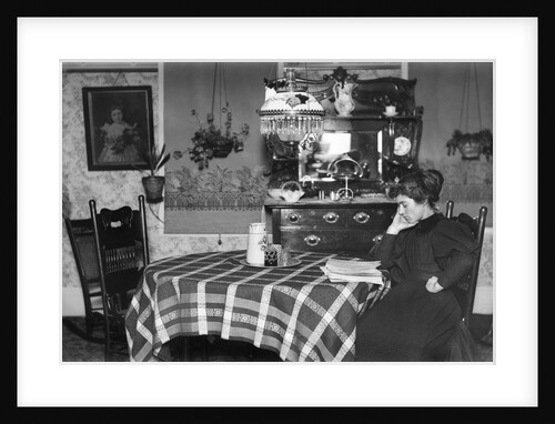 A woman reads at the dining table, ca. 1900. by Anonymous