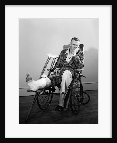1950s man in wheelchair leg in cast with crutches at side looking at camera by Anonymous