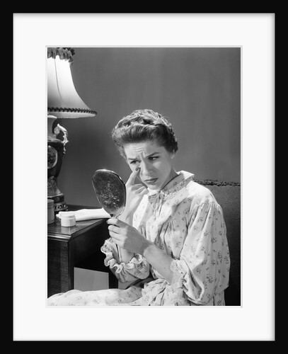 1950s 1960s woman in nightgown holding mirror look at eye wrinkles aging beauty cosmetic serious concerned expression by Anonymous
