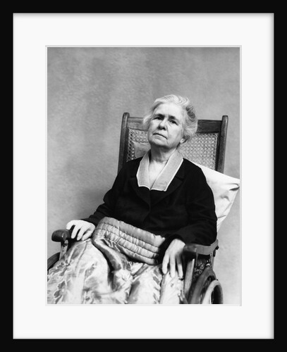 1930s geriatric sad senior old woman in wheelchair looking at camera crippled by age with comforter blanket over legs by Anonymous