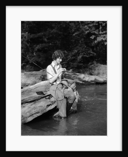 1920s 1930s woman sitting on rock by side of stream wearing waders putting fly on tippet by Anonymous