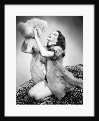 1950s young woman wearing sexy lingerie kneeling on leopard skin holding fluffy dog by Anonymous