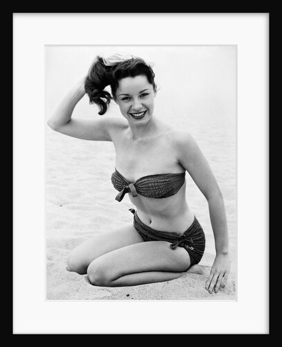 1950s young woman wearing bikini bathing suit kneeling on beach looking at camera by Anonymous