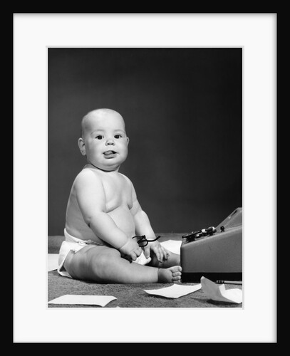 1950s 1960s baby in diaper sticking out tongue holding glasses sitting before adding machine looking at camera by Anonymous