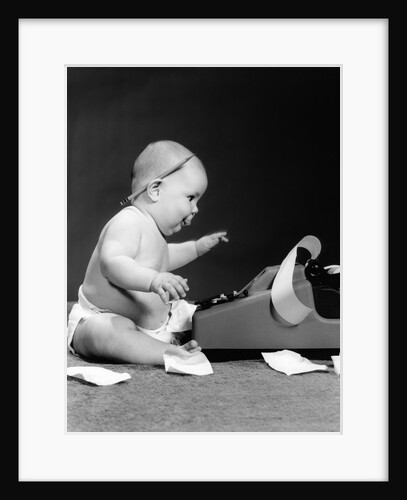 1960s side view of chubby baby seated behind adding machine with pencil behind ear & tape scattered on floor by Anonymous