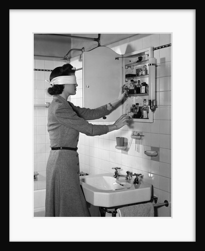 1940s woman wearing blindfold reaching into bathroom medicine cabinet by Anonymous