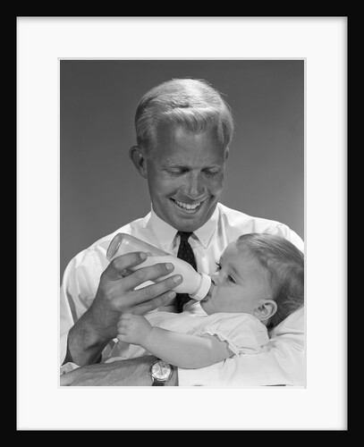 1960s smiling blond father feeding child milk in glass baby bottle by Anonymous