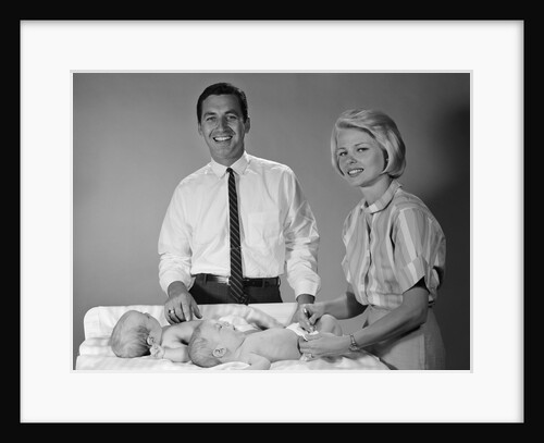 1960s smiling mother and father with twin babies on diaper changing table looking at camera by Anonymous