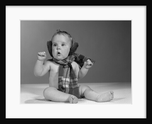 1960s baby sitting up wearing winter ear muffs and plaid woolen scarf around neck by Anonymous
