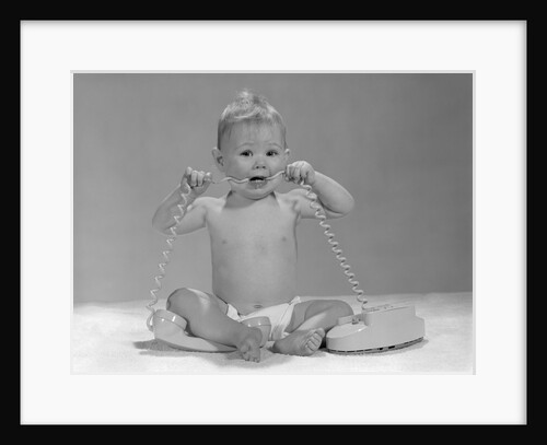 1960s blond baby sitting up looking at camera chewing on telephone cord by Anonymous