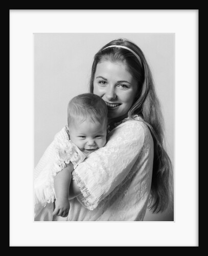 1970s side view portrait of smiling mother in nightgown holding baby looking at camera by Anonymous