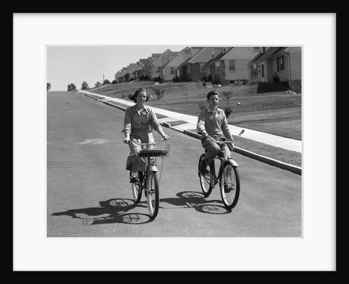 1950s teen boy girl couple riding bikes down residential street by Anonymous