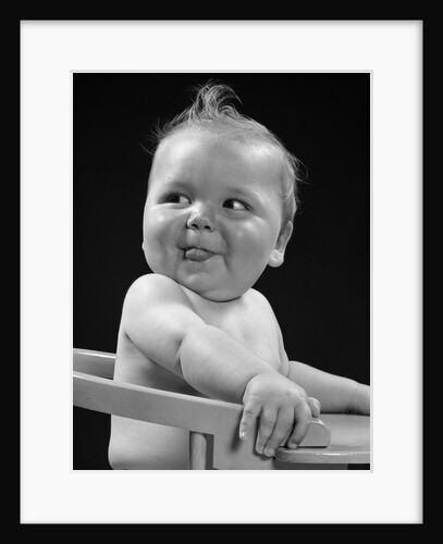 1950s 1940s baby in high chair head turned to one side with tongue sticking out funny facial expression by Anonymous