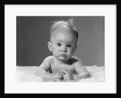 1960s portrait baby lying on stomach with messy hair and bulging eyes looking at camera by Anonymous