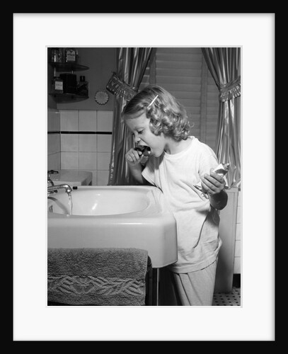 1950s little blond girl in pajamas standing at bathroom sink brushing her teeth toothpaste and toothbrush in hand by Anonymous