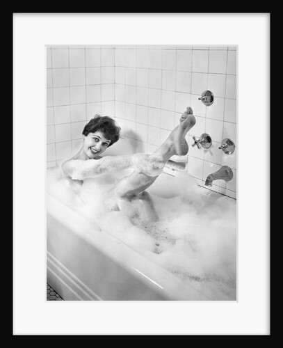 1950s sexy smiling woman taking a soap suds bubble bath in tub looking at camera by Anonymous