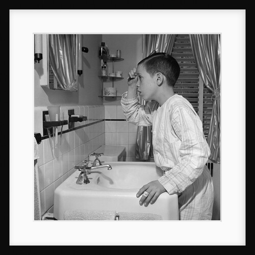 1950s boy combing hair looking in bathroom sink mirror by Anonymous