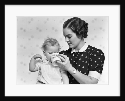 1930s woman mother giving baby daughter drink from mug by Anonymous