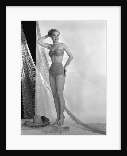 1950s glamour girl looking at camera posed in studio draped in fishing net wearing two piece bathing suit by Anonymous
