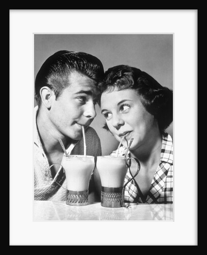 1940s 1950s romantic teenage couple boy and girl head to head drinking ice cream sodas by Anonymous