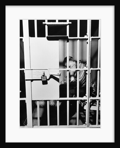 1960s man seated on bench in jail cell with head in hand looking downward by Anonymous
