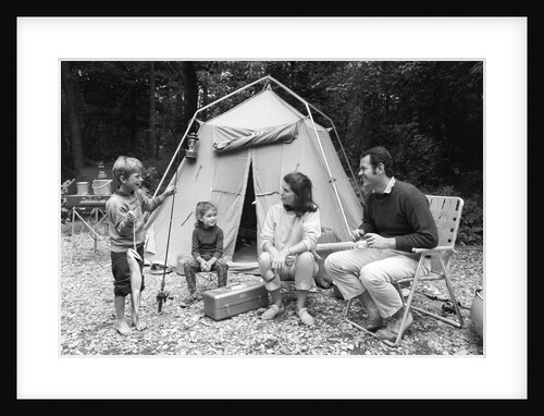 1970s family of four sitting in front of tent in woods son holding fishing pole in one hand & big fish in other by Anonymous