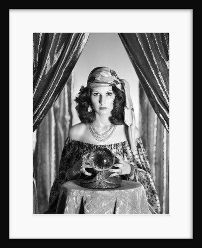 1970s gypsy woman between sparkly curtains with hands around crystal ball staring into camera by Anonymous