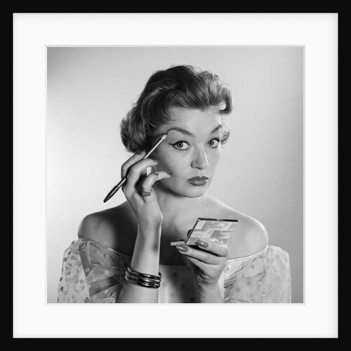 1950s 1960s woman looking at camera applying makeup eye brow pencil holding compact mirror by Anonymous