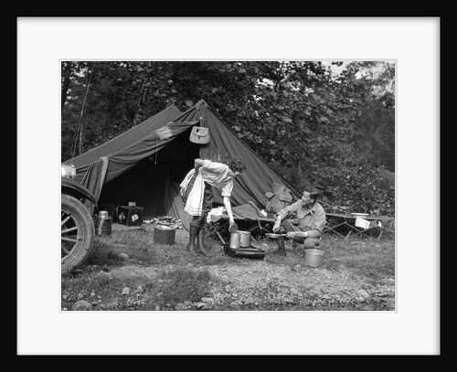 1920s couple man woman on fishing camping trip vacation at campsite man cooking over fire by Anonymous
