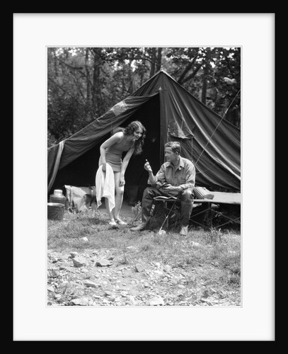 1920s camping couple man sitting by tent with fishing rod woman standing wearing bathing suit by Anonymous