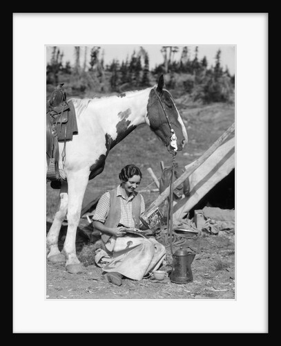 1920s 1930s woman sitting outside of tent next to pinto horse pouring syrup from tin onto pancakes wearing vest and chaps glacier park by Anonymous